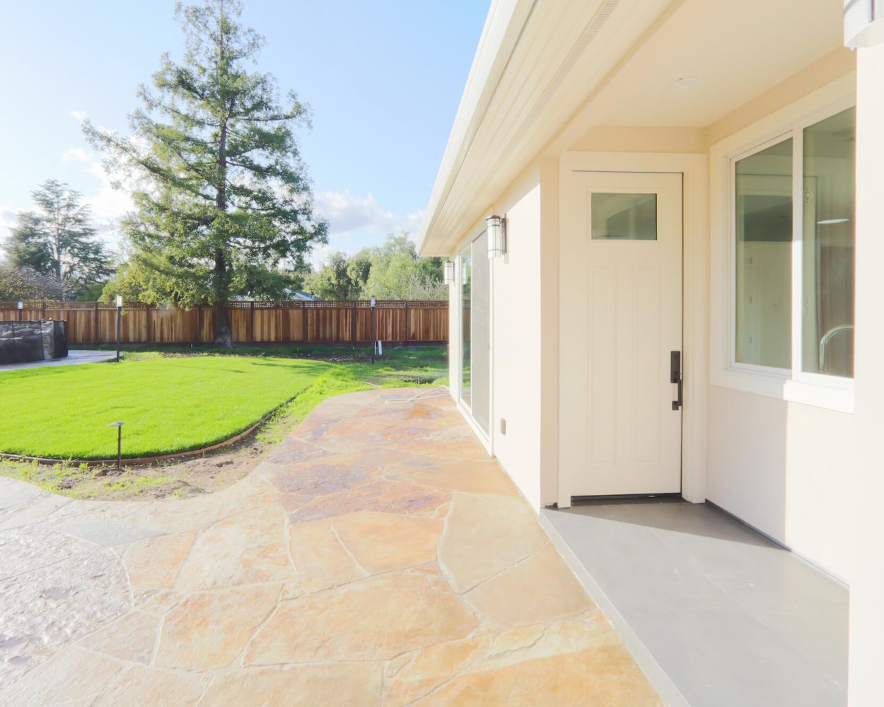 Exterior of additional dwelling unit with private entrance, patio, and fenced backyard in sunlight.