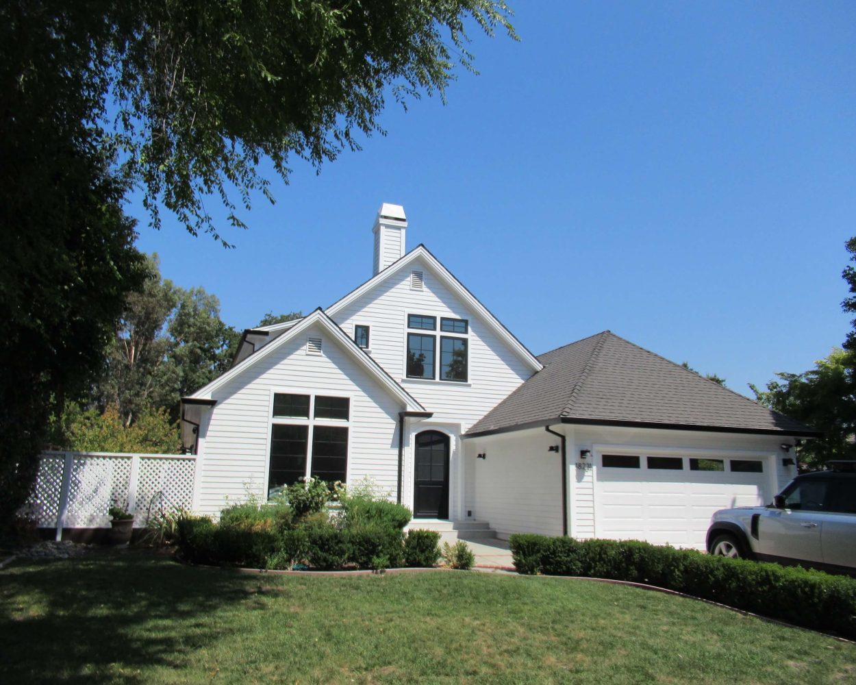 White two-story home exterior renovation with front lawn, attached garage, large windows, and landscaped yard.
