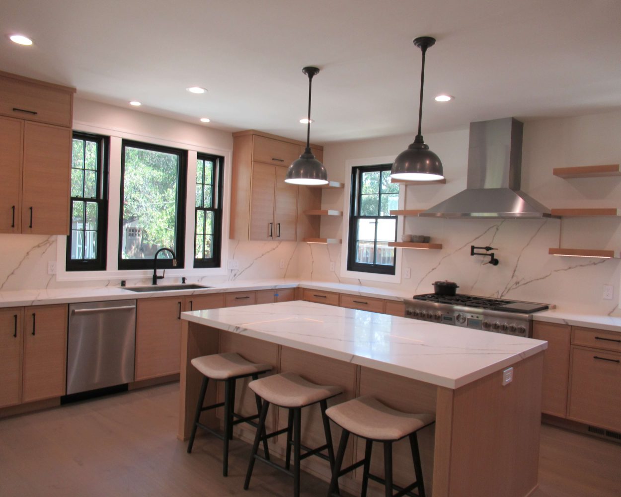 Minimalist wood kitchen featuring floating shelves, marble countertops, and industrial black dome pendant lights.