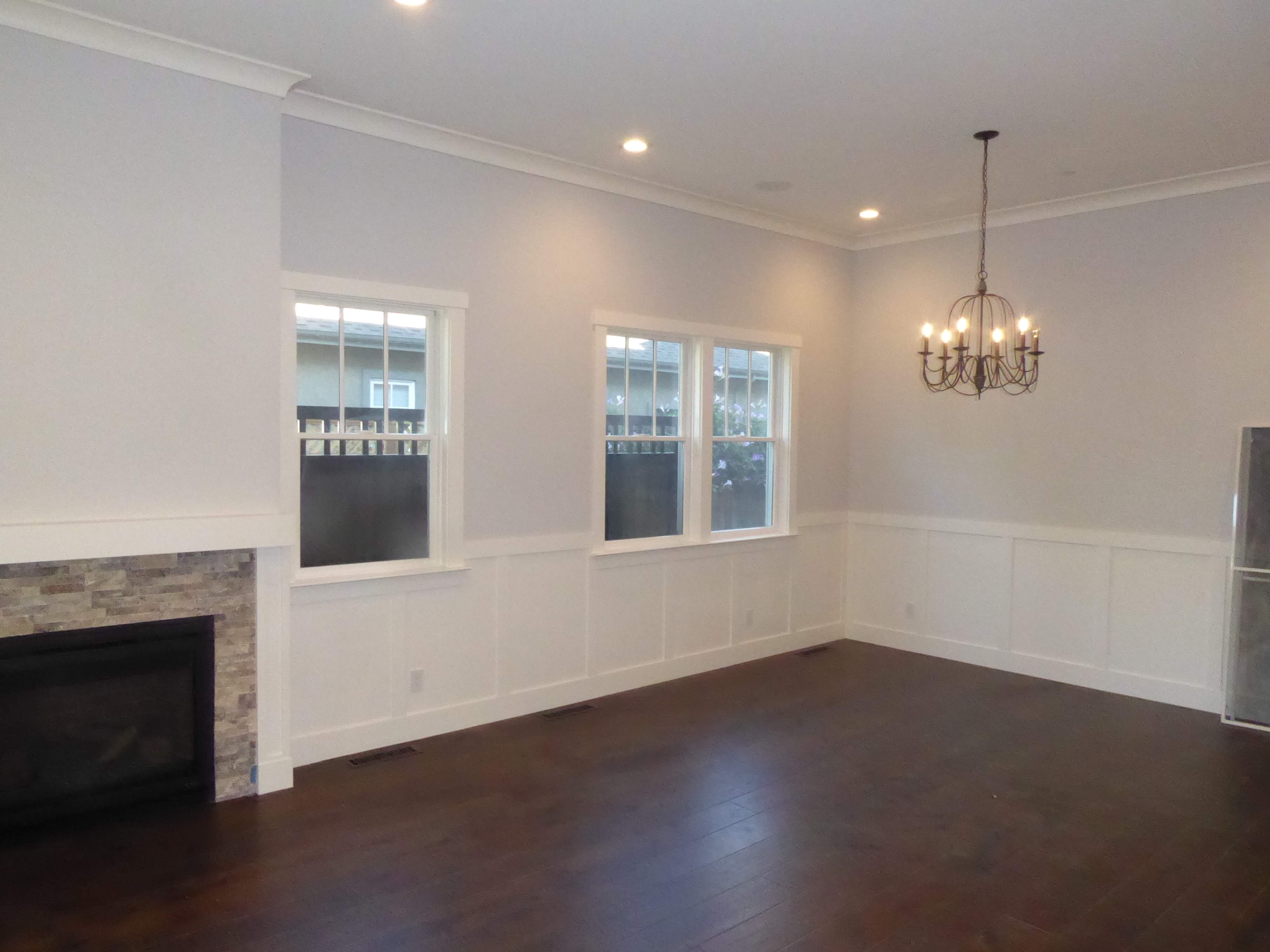 Living room of new construction home with fireplace, dark wood floors, white wainscoting, recessed lighting, and chandelier.